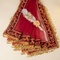 A deep red and gold embroidered dupatta with tassels, featuring a decorative white feather and gold heart brooch, laid out on a light beige background.