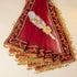 A deep red and gold embroidered dupatta with tassels, featuring a decorative white feather and gold heart brooch, laid out on a light beige background.